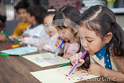 group of Cute little girl and boy student blowing color pen painting together with nursery teacher in classroom school . Happy Stock Photo