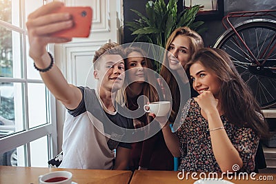 Group of cute teenagers taking selfie with cellphone while sitting in a restaurant with interior in retro style Stock Photo