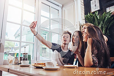 Group of cute teenagers taking selfie with cellphone while sitting in a restaurant with interior in retro style Stock Photo