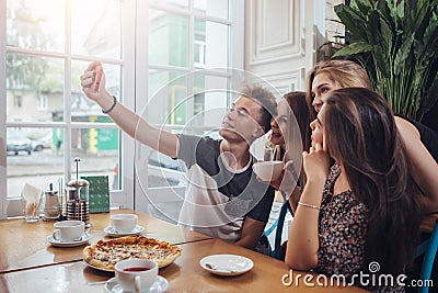 Group of cute teenagers taking selfie with cellphone while sitting in a restaurant with interior in retro style Stock Photo