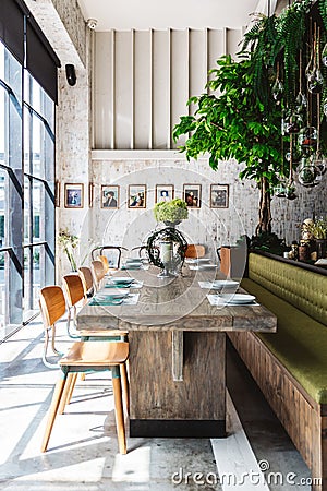 Group dining table set decorated with green sofa, wooden table, wooden chairs, green plant and white scratch texture wallpaper. Stock Photo