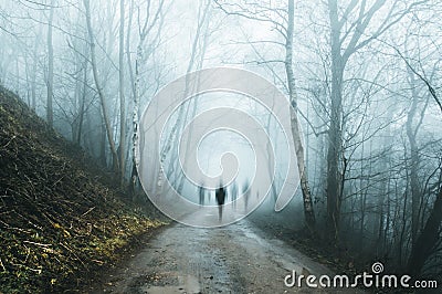 A group of eerie ghostly figures emerging from the fog on a spooky forest road in winter. With a high contrast photoshop edit Stock Photo