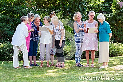 Group of elderly ladies at a care home enjoying a stimulating creative art class outdoors in a garden or park. Stock Photo