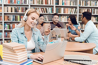 Group of ethnic multicultural students in library. White girl working on laptop with headphones. Stock Photo