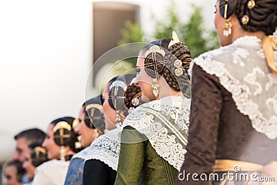 A group of falleras in a row seen from behind. Dresses with tablecloth and typical hairstyle of the fallas with their jewels Editorial Stock Photo