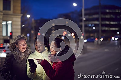 Group Of Female Friends On City Street At Night Ordering Taxi Using Mobile Phone App Stock Photo