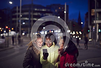 Group Of Female Friends On City Street At Night Ordering Taxi Using Mobile Phone App Stock Photo