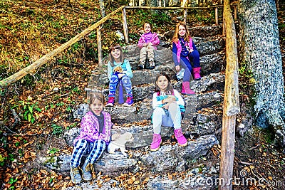 Group of five little girls sitting on the stone staps and playing with puppies in the forest Stock Photo