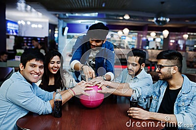 Group of five south asian peoples having rest and fun at bowling club, sitting on table and drinking soda drinks at glass bottles Stock Photo