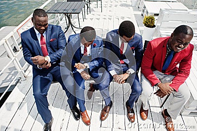 Group of four african american happy succesfull mans at suit. Rich black business mans sitting at chairs and looking at watches. Stock Photo