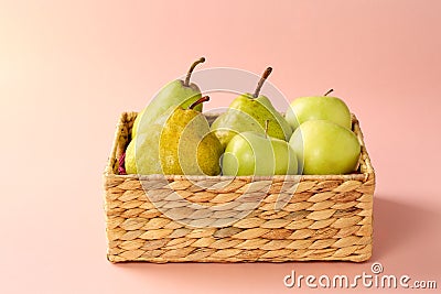 Group of fresh, ripe and juicy apples and pears in a water hyacinth basket against pink background Stock Photo