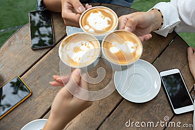 Group of friends cheers with latae cup in cafe bar with phone on table sitting outdoor at cafe - Young girl group having fun Stock Photo