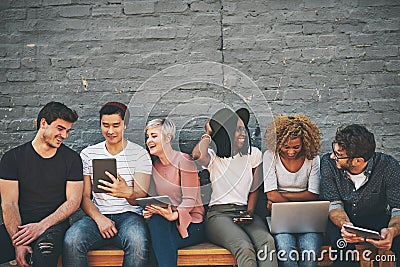 Group of friends on digital devices and social media sitting together while smiling and talking. Technology obsessed Stock Photo