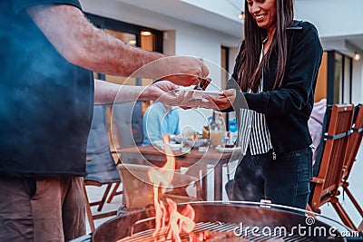 A group of friends and family barbecue together in the evening on the terrace in front of a large modern house Stock Photo