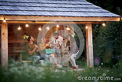 A group of friends having a good time at birthday party at the cottage porch. Vacation, nature, cottage, celebration Stock Photo