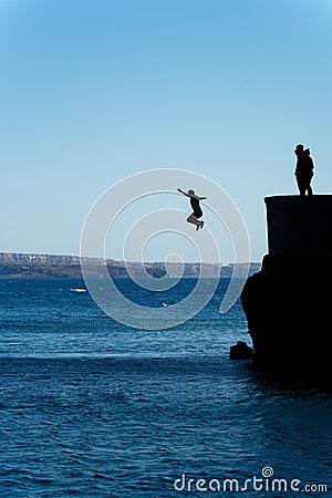 Group of friends jumping into mediterranean sea from rock cliff Stock Photo