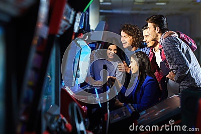 A group of friends playing arcade machine. Stock Photo