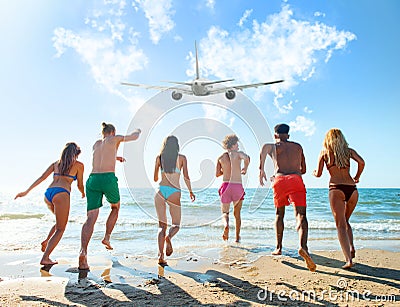 Group of friends run to the sea with an aircraft in the sky. Concept of travel and summer Stock Photo
