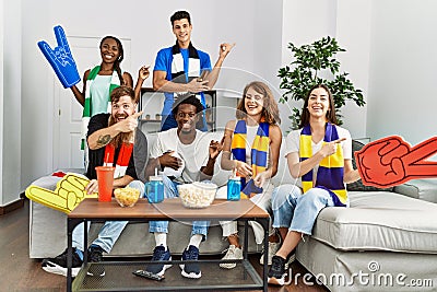 Group of friends supporting football team watching tv al home sitting on the sofa smiling happy pointing with hand and finger to Stock Photo