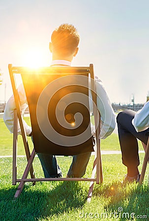 Group of handsome businessmen relaxing and talking about life while sitting on folding chair at park Stock Photo