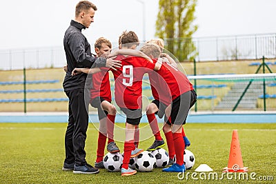 Group of happy boys making sports huddle. Smiling kids standing together with coach on grass sports field Stock Photo