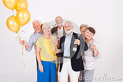 Happy senior friends holding yellow balloons and standing in white interior Stock Photo