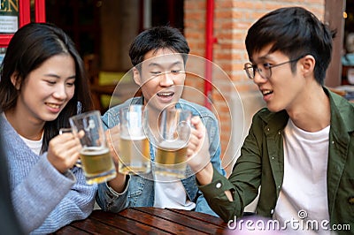 Group of happy young Asian friends are enjoying drinking beers and talking at a bar together Stock Photo