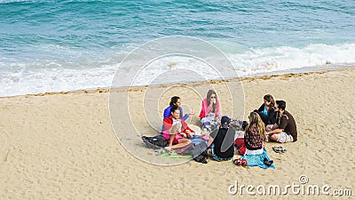 Group of happy young people sitting in a circle on the sandy beach Editorial Stock Photo