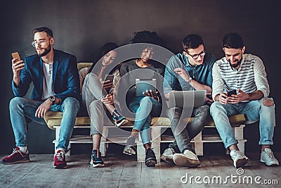 Group of happy young people sitting on sofa and using digital tablet and laptop Stock Photo