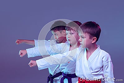 Group of kids, different boys, taekwondo athletes in white doboks in action on lilac color background. Concept Stock Photo