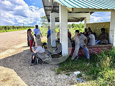 A group of locals and one tourist waiting at a remote bus stop for the local bus heading to Placencia along the side of the highwa Editorial Stock Photo