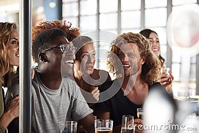 Group Of Male And Female Friends Celebrating Whilst Watching Game On Screen In Sports Bar Stock Photo