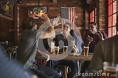 Group Of Male Friends Celebrating Whilst Watching Game On Screen In Sports Bar Stock Photo