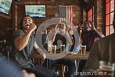 Group Of Male Friends Celebrating Whilst Watching Game On Screen In Sports Bar Stock Photo