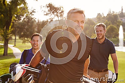 Group Of Male Golfers Walking Along Fairway Carrying Bags Stock Photo