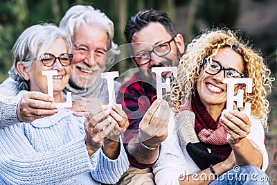 Group of mixed ages generations people smiling and showing blocks letters with life word - happy lifestye enjoying the outdoor Stock Photo