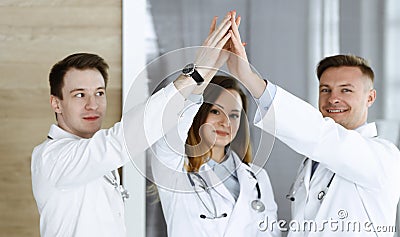 Group of modern doctors standing as a team while joining hands or giving five to each other. Physicians ready to examine Stock Photo