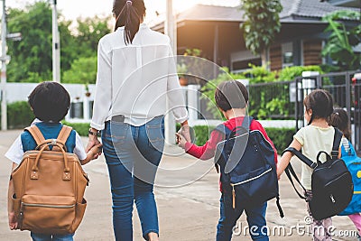 Group of mother and kids holding hands going to school with schoolbag. Mom bring children walk to school by bus together with Stock Photo