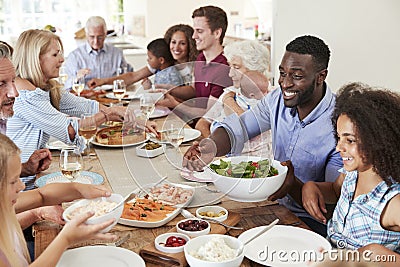 Group Of Multi-Generation Family And Friends Sitting Around Table And Enjoying Meal Stock Photo