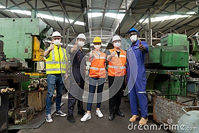 Group of multiethnic engineer with workers giving thumbs up and wearing surgical mask to prevent covid-19 in manufacturing factory Stock Photo
