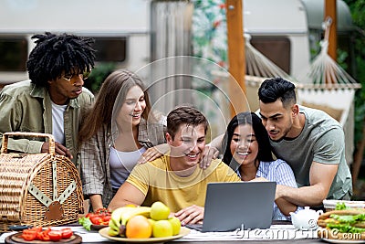 Group of multiracial millennial friends using laptop on autumn camping trip to countryside, chatting online, having fun Stock Photo