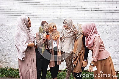 Group of Muslim Asian women wearing hijab standing and having conversation by white brick wall Editorial Stock Photo