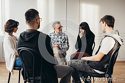 Group of people of different ages sits in a circle during a meeting with a professional therapist Stock Photo