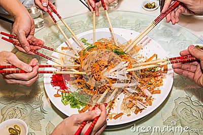 A group of people mixing and tossing Yee Sang dish with chop sticks. Yee Sang is a popular delicacy taken during Chinese New Stock Photo