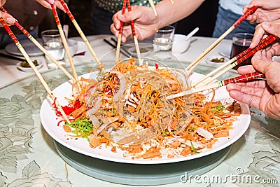 A group of people mixing and tossing Yee Sang dish with chop sticks. Yee Sang is a popular delicacy taken during Chinese New Stock Photo