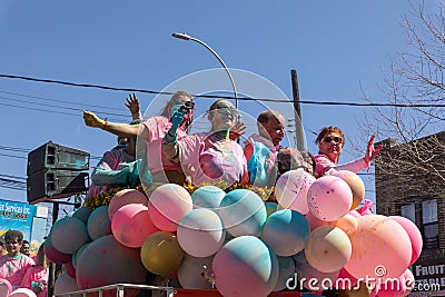 A group of people in pink shirts riding a float of balloons on the street Editorial Stock Photo