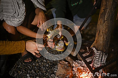 Group of people sitting near burning bonfire and drinking some beer while camping on weekend holiday. Stock Photo