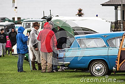 Group of people stand in raincoats with an umbrella talking in the rain at a classic car show Editorial Stock Photo