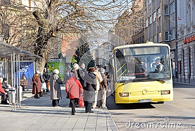 Group of people waiting in queue to enter local city bus on bus stop station Editorial Stock Photo