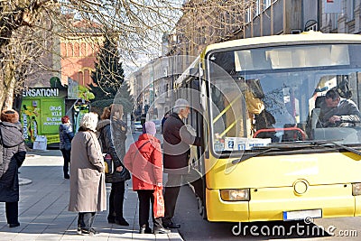 Group of people waiting in queue to enter local city bus on bus stop station Editorial Stock Photo